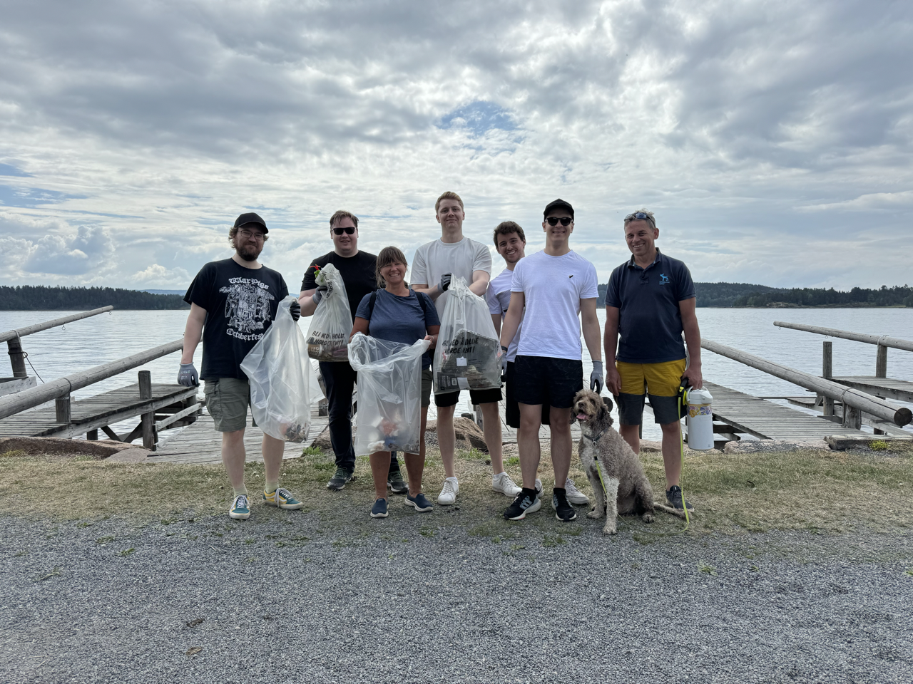 8 people and a dog in front of the Oslo fjord, equipped with gloves and trash bags in the middle of a beach cleanup